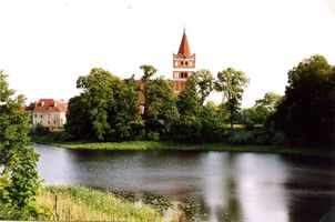 Friedland (Ostpr.), Kreis Bartenstein Friedland (Правдинск), Kirche mit Blick von der ehemaligen Kreisstraße 131 von Lisettenfelde kommend über den Mühlenteich 
